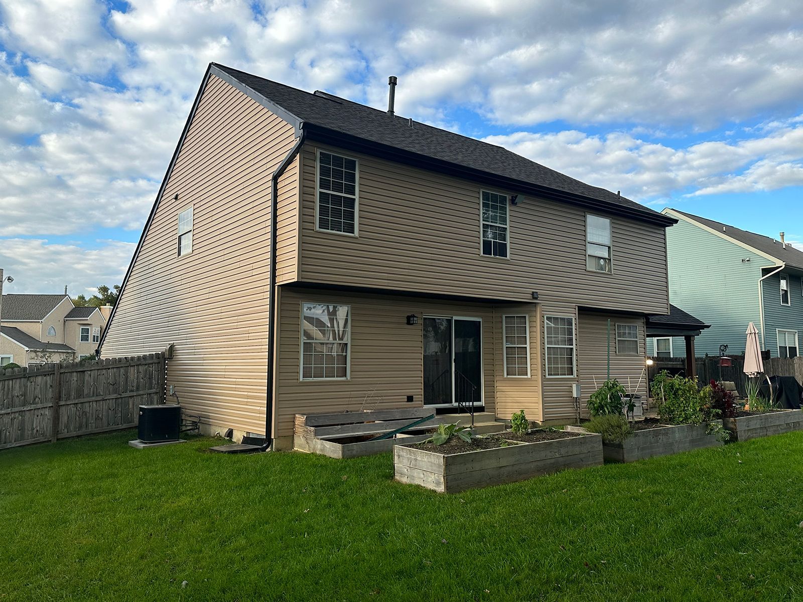 Back of a two-story beige house with a green lawn and concrete garden beds. Overcast sky with hints of blue.