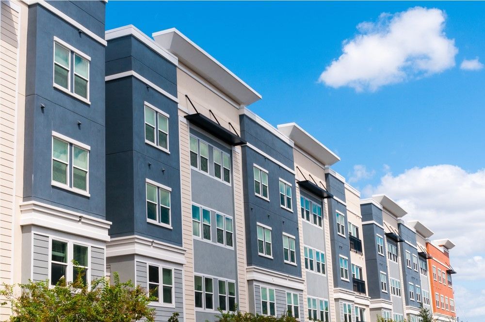 Multi-story apartment building with blue, gray, and white exterior paint under a blue sky with clouds.
