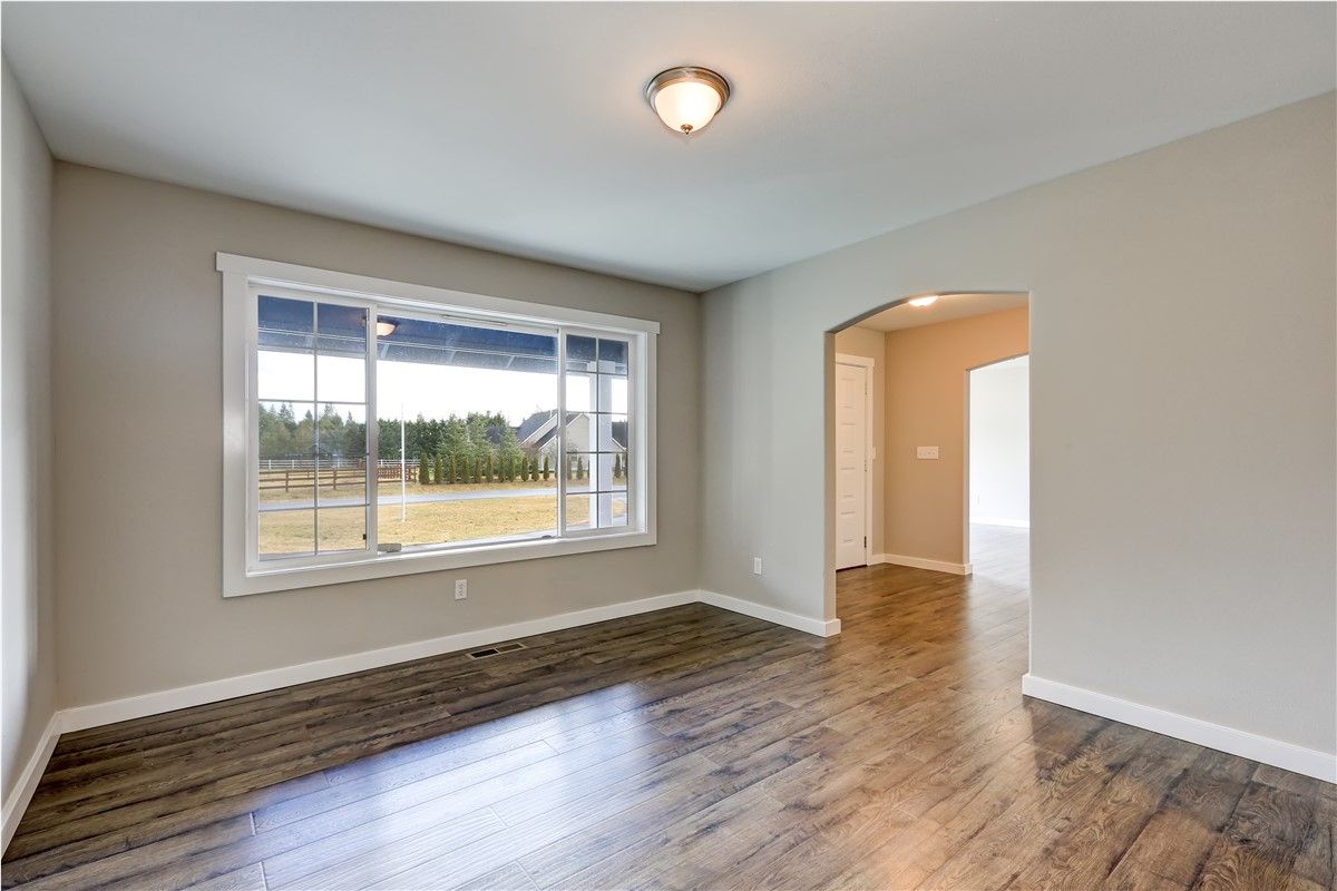 Empty room with hardwood floor, large window, and an arched doorway. Neutral wall color.