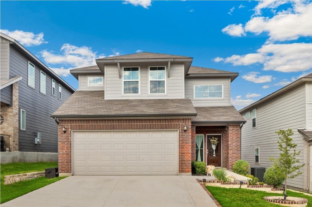 Two-story house with gray siding, red brick accents, and a two-car garage against a blue sky.