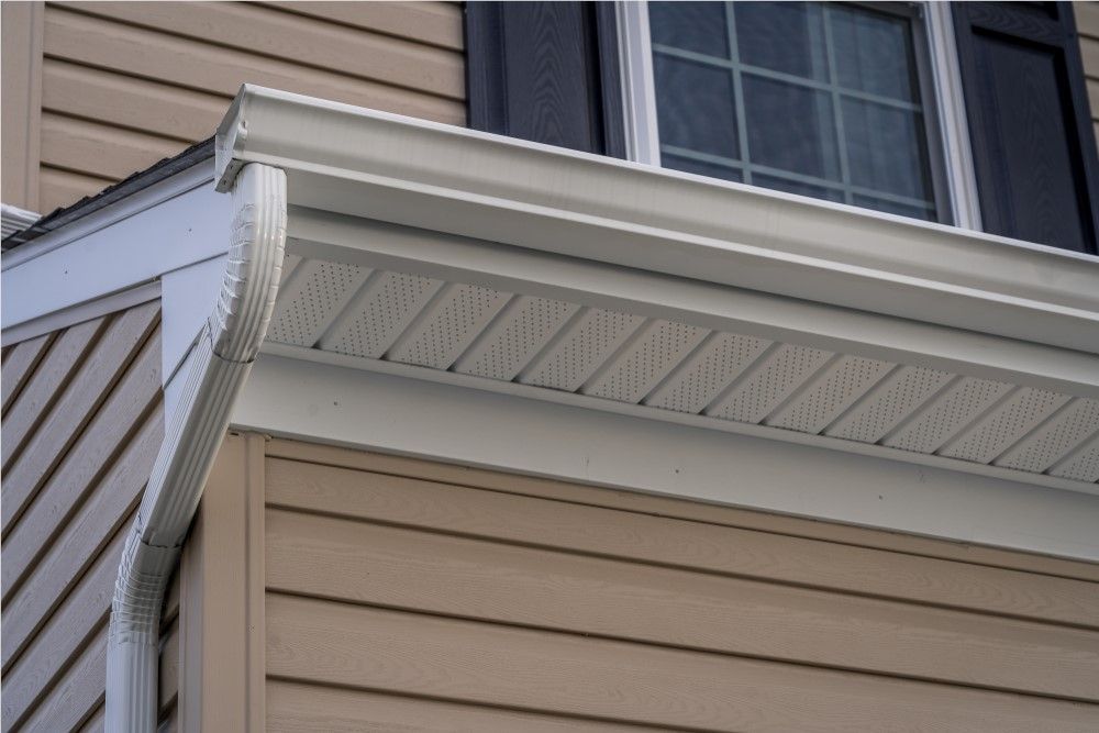 Beige house exterior with white gutters and soffit, a window with dark shutters, and light brown siding.
