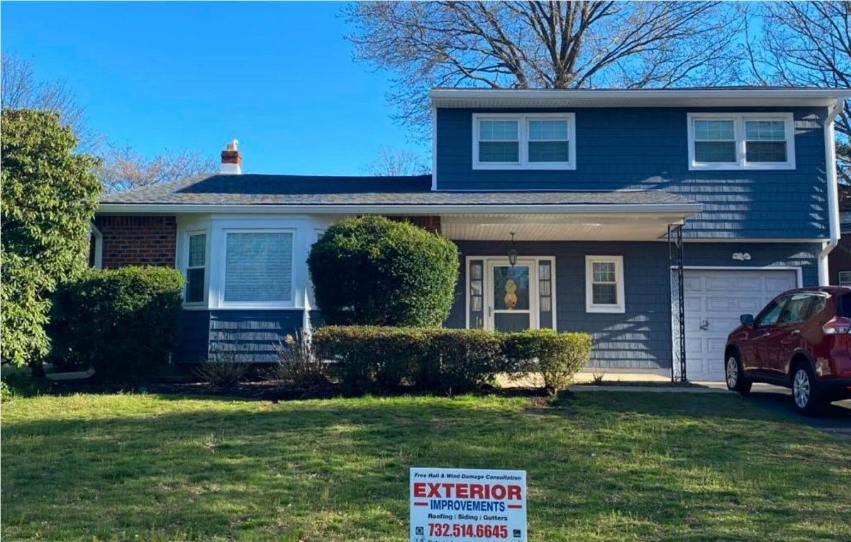 A two-story house with blue siding and a red car parked in the driveway. The house is in a suburban setting with green grass.