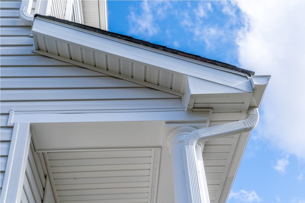 White house exterior with a gutter system against a blue sky. Details include siding, soffit, and downspout.