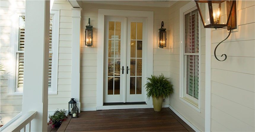 Beige exterior with double glass doors, lit lanterns, and a potted fern on a wooden porch.