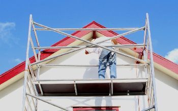 A man is painting the side of a house on a scaffolding.