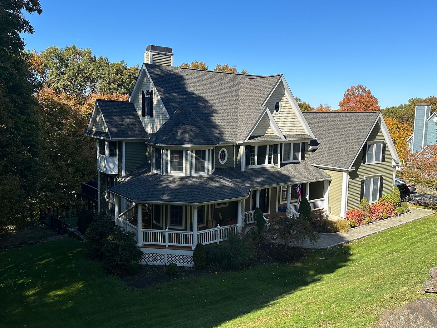 Green Victorian house with porch, surrounded by trees with fall foliage, set on a green lawn under a blue sky.