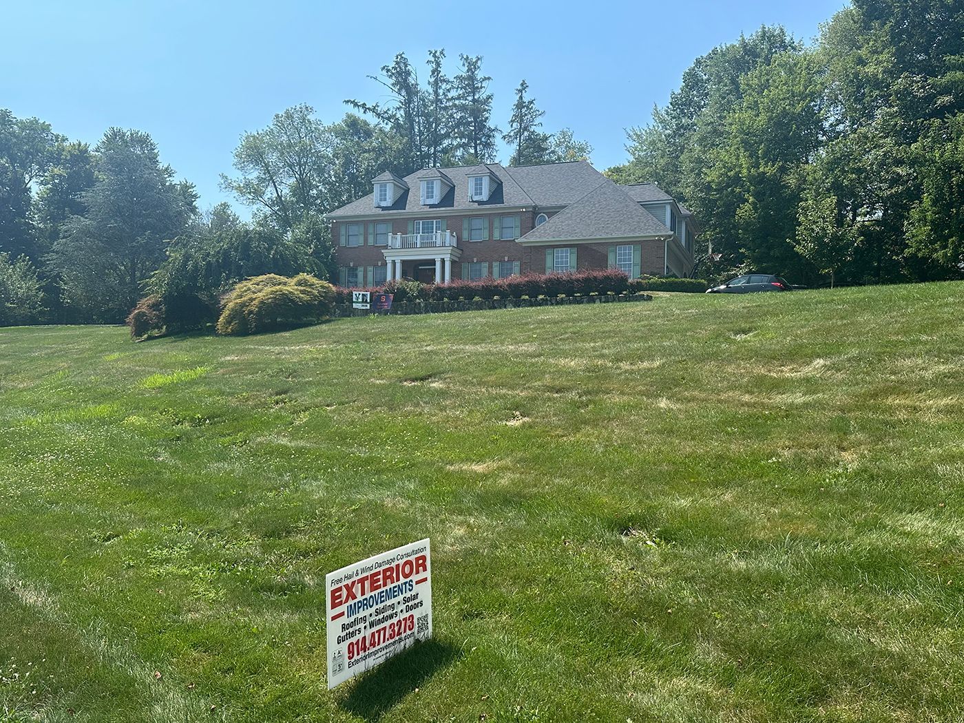 A brick mansion sits atop a grassy hill with a 