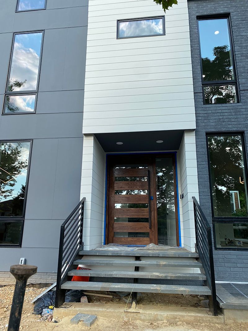 Modern house exterior with gray and white panels, dark brick accents, and a brown front door, steps leading to the entrance.