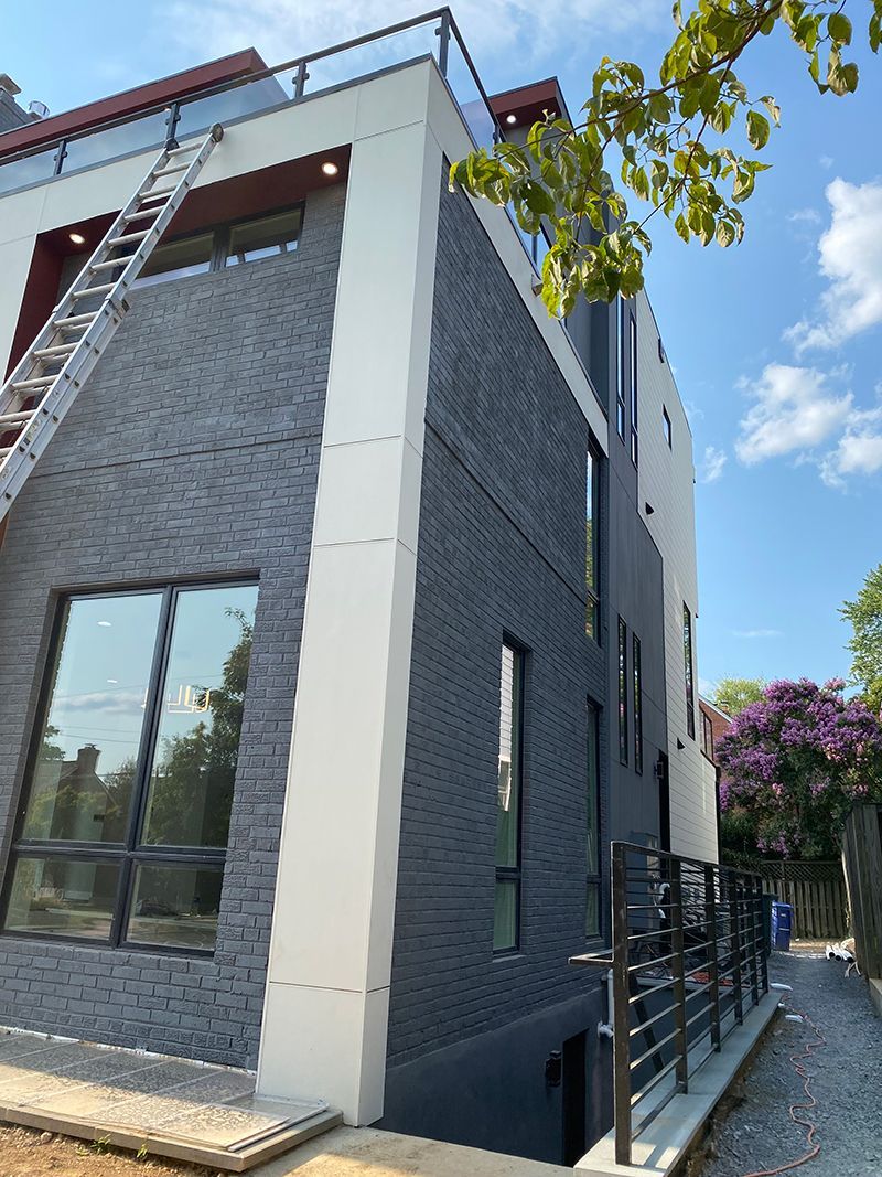 Modern multi-story building with dark gray brick facade, white trim, and a ladder against the side.