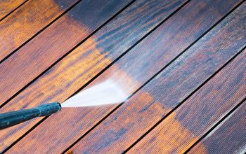 A person is using a high pressure washer to clean a wooden deck.