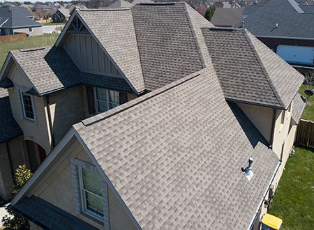 Tan house with a multi-faceted gray shingled roof under a blue sky.