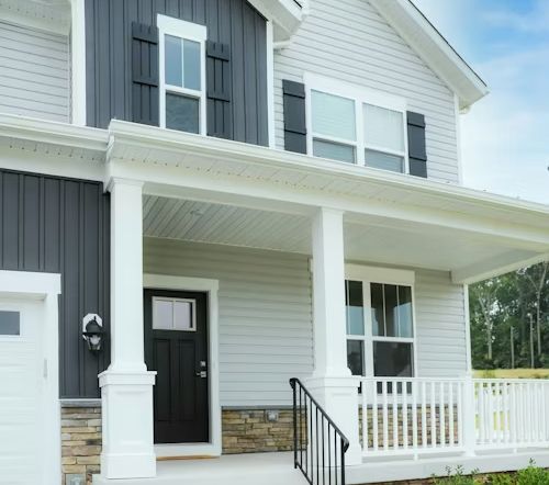 A modern two-story home with light gray siding, dark gray vertical accents, a stone base, and a white front porch.
