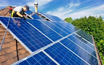 A man is installing solar panels on the roof of a house.