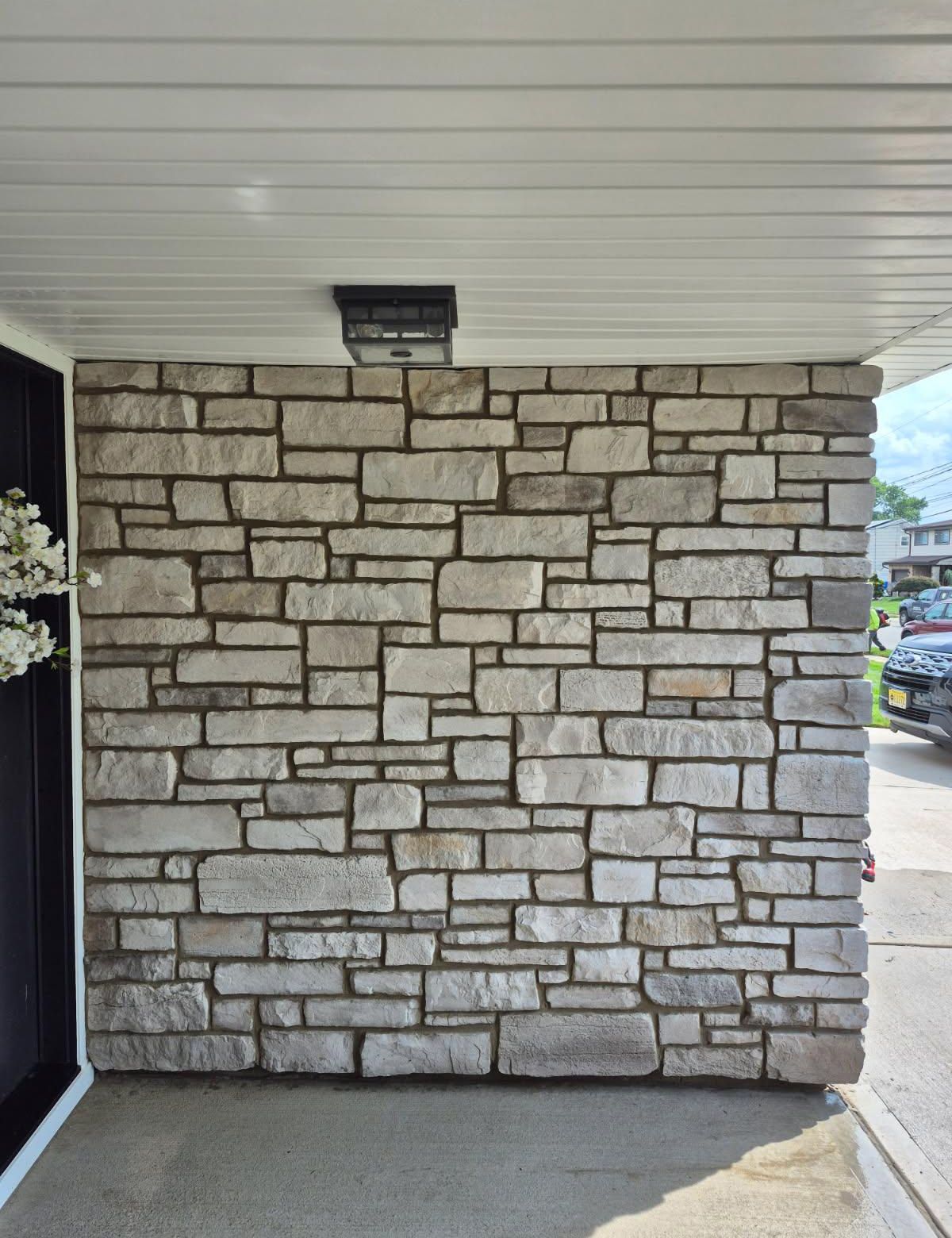 Stone veneer wall on a porch with a black light fixture.