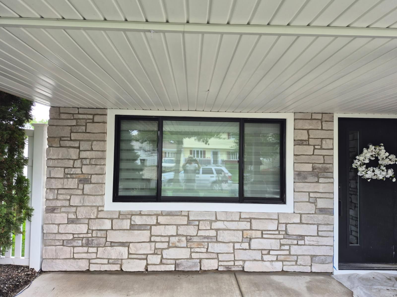 Stone veneer facade with black-framed window and white ceiling, door with wreath to the right.