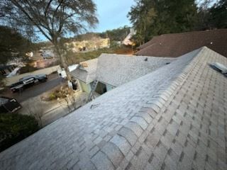 Rooftop view of gray shingle roof. Buildings, trees, and street in the background.