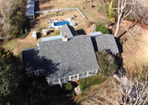 Aerial view of a house with a gray roof, a blue pool, and surrounding trees.