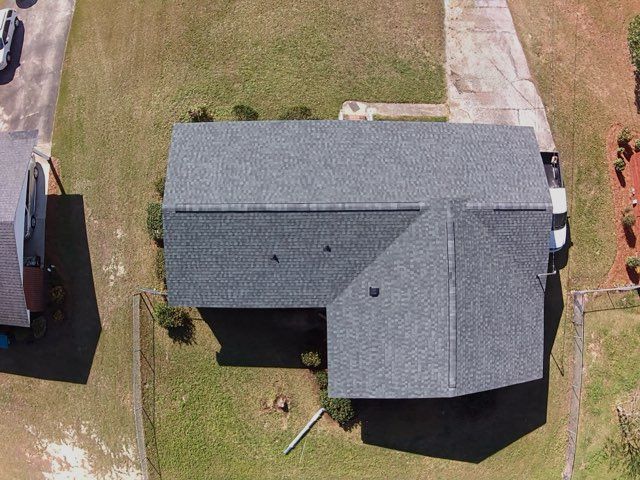 An overhead, aerial view of a gray shingled roof on a residential house situated on a grassy lot.