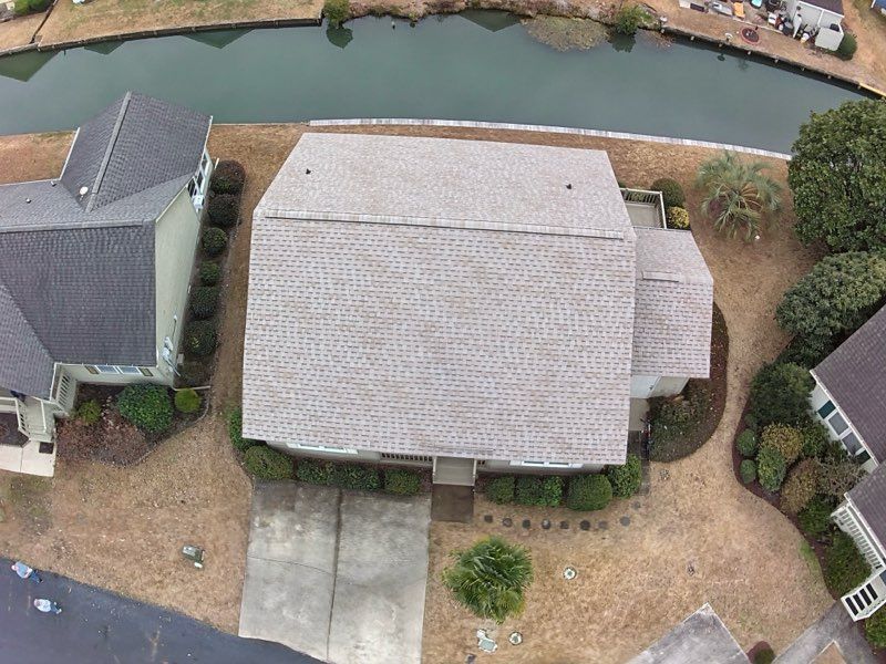 Overhead view of a house with a gray roof, brown yard, and a canal in the background.