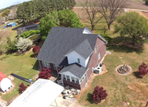 Aerial view of a two-story brick and white house with a dark roof surrounded by a lawn, trees, and an outbuilding.