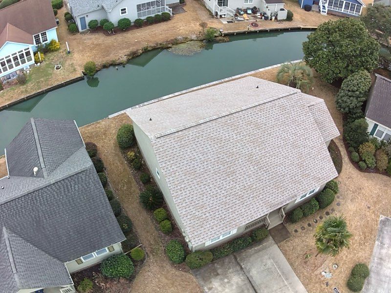 Aerial view of a house with a light gray roof and surrounding greenery, located near a waterway.