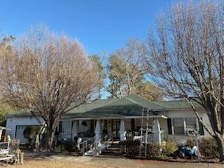 White house with green roof, carport, porch, and bare trees under a clear blue sky.