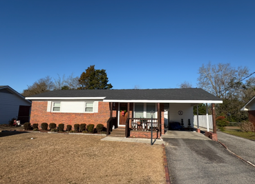 Green asphalt shingle roof, treeline in background.