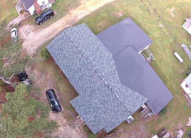 Roofing workers on a house; tent and equipment in yard; blue sky.