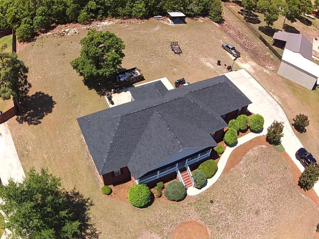 Green asphalt shingle roof, treeline in background.