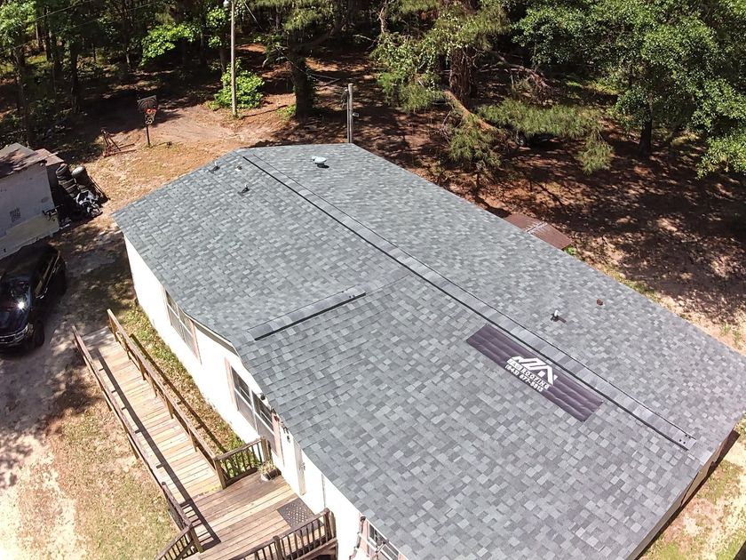 Roofing workers on a house; tent and equipment in yard; blue sky.