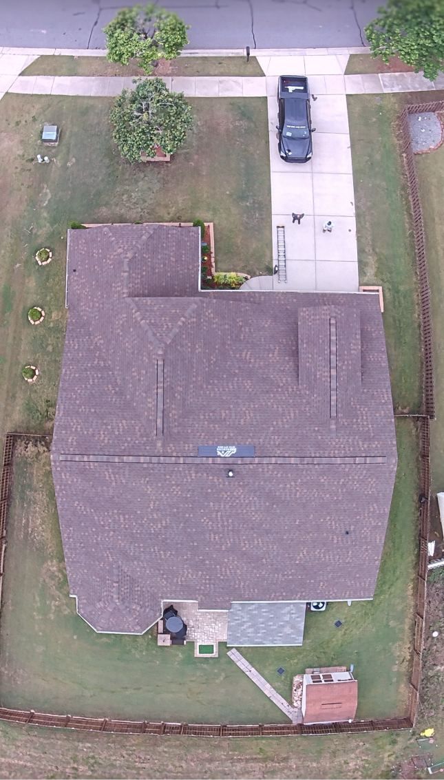 Aerial view of a house with a gray roof, small front yard, driveway, and parked car.