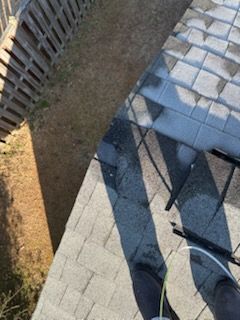 View from rooftop, gray shingles, wooden fence, brown grass, shadows cast in sunlight.