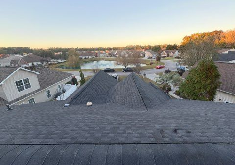 View from a roof of a neighborhood with a pond, trees, and houses; a clear sky at dusk.