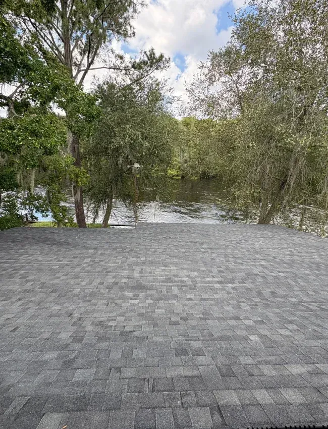 Dark tiled roof with chimney and two skylights against a blue sky.