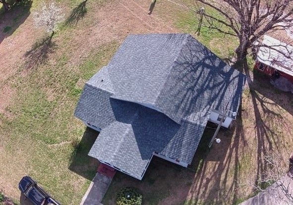 Aerial view of a house with a gray roof and shadows cast by a large tree.