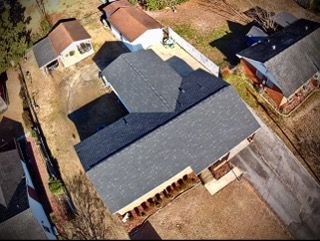 Overhead view of several houses with dark gray roofs, brown yards, and a paved road.