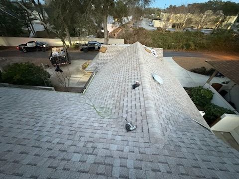 A roof under construction, covered in gray shingles. Tools and materials are scattered on the roof.