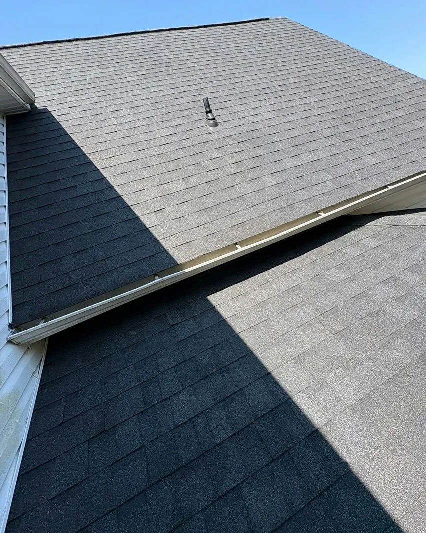 Close-up of a house roof with dark gray shingles on a sunny day.