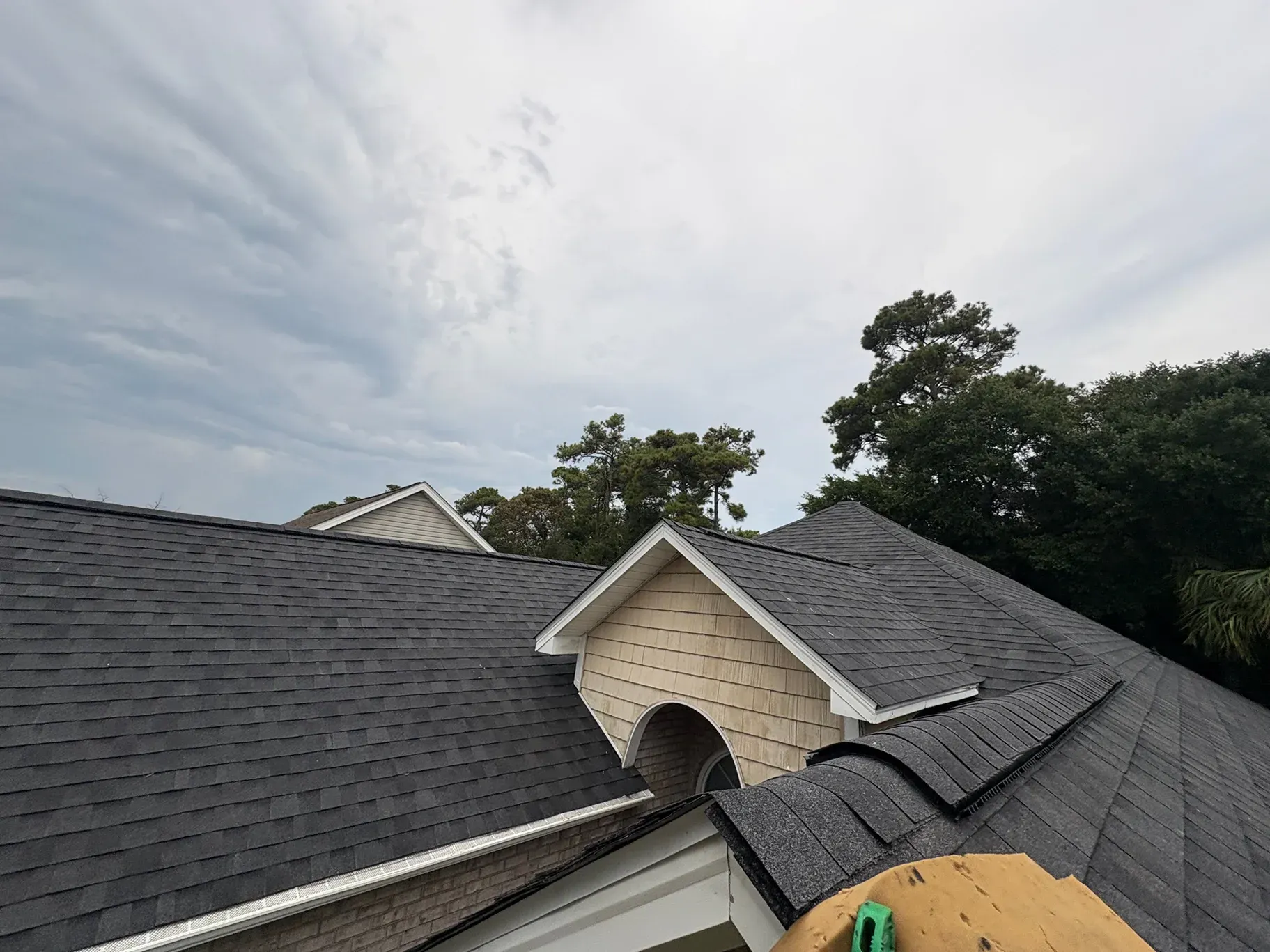 Dark asphalt shingle roof with a light beige gable against a cloudy sky.