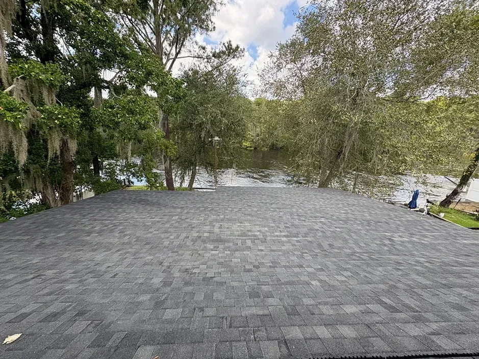 Gray shingle roof overlooking a body of water with trees on the banks under a cloudy sky.