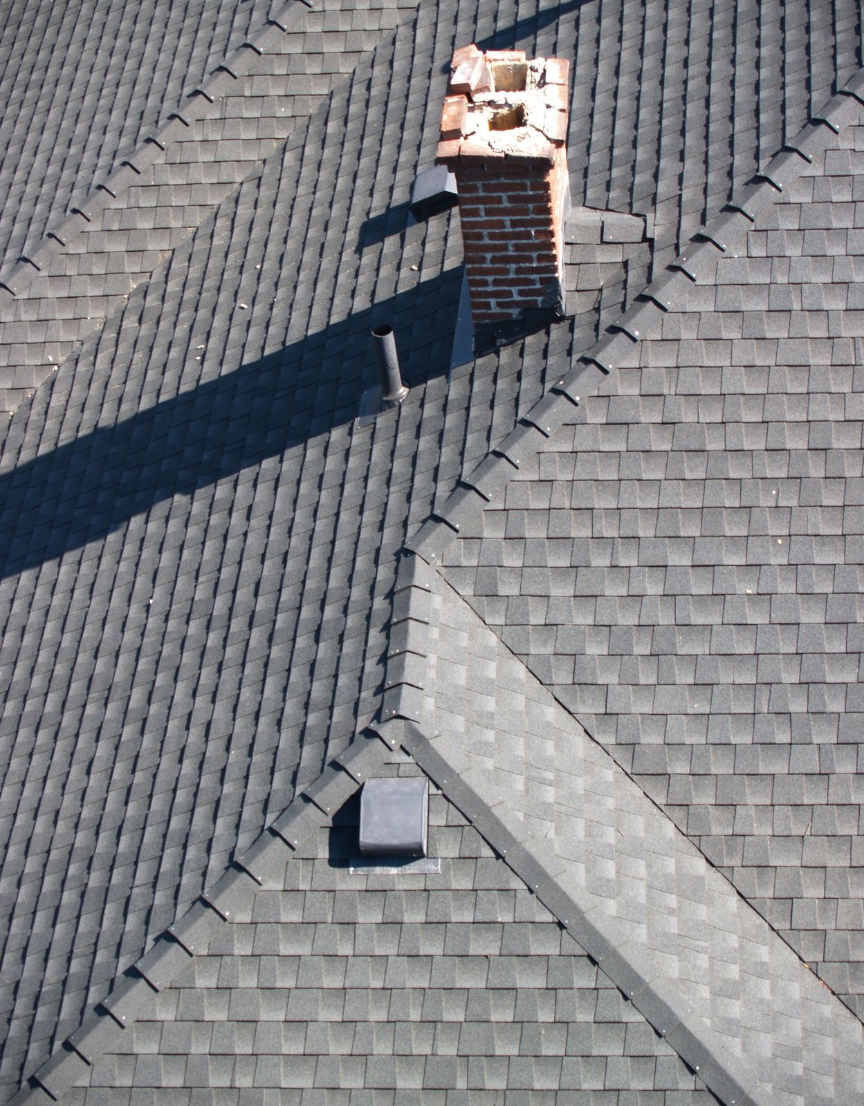 Dark gray shingled roof with a brick chimney and a small vent.