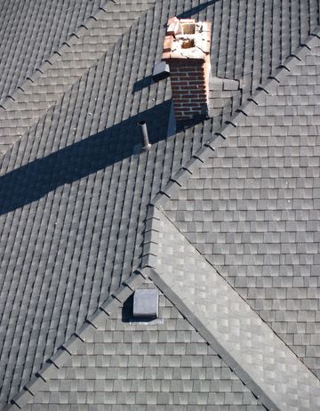 Dark gray shingled roof with a brick chimney and a small vent.