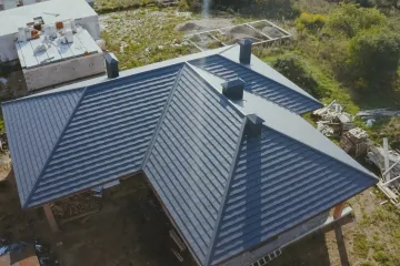 Dark gray metal roof with three black chimney stacks on a wooden building, aerial view.