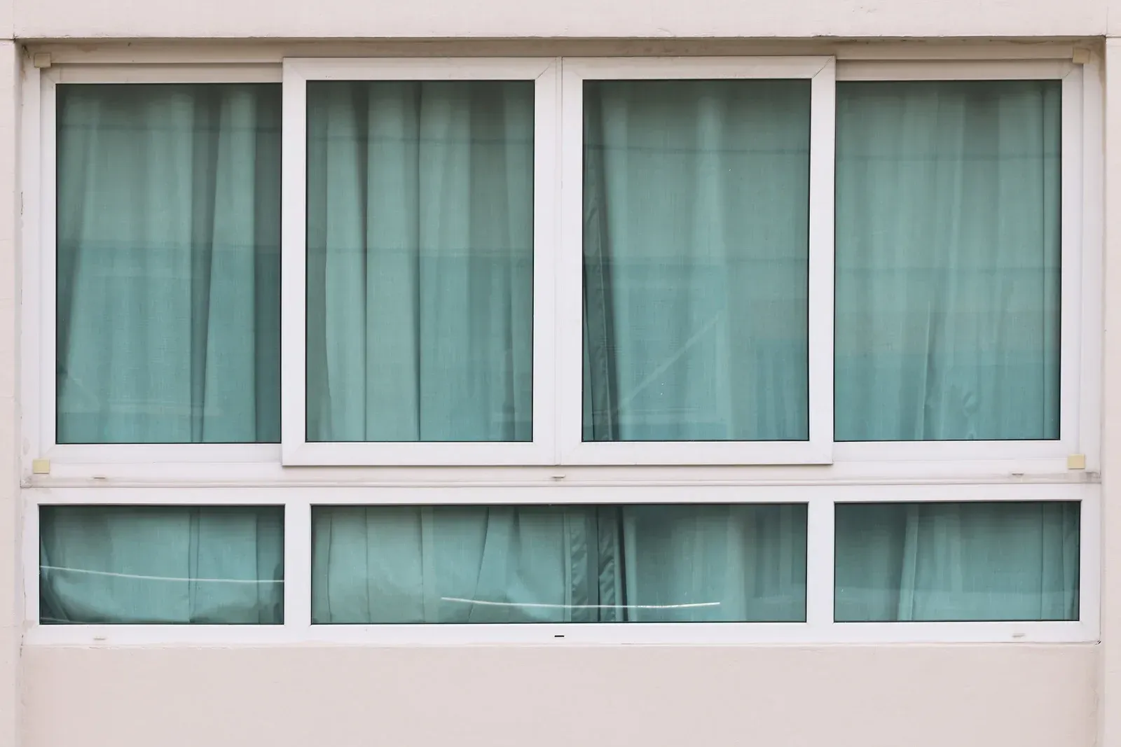 White-framed window with four rectangular panes and two smaller panes below. Teal curtains are visible behind the glass.