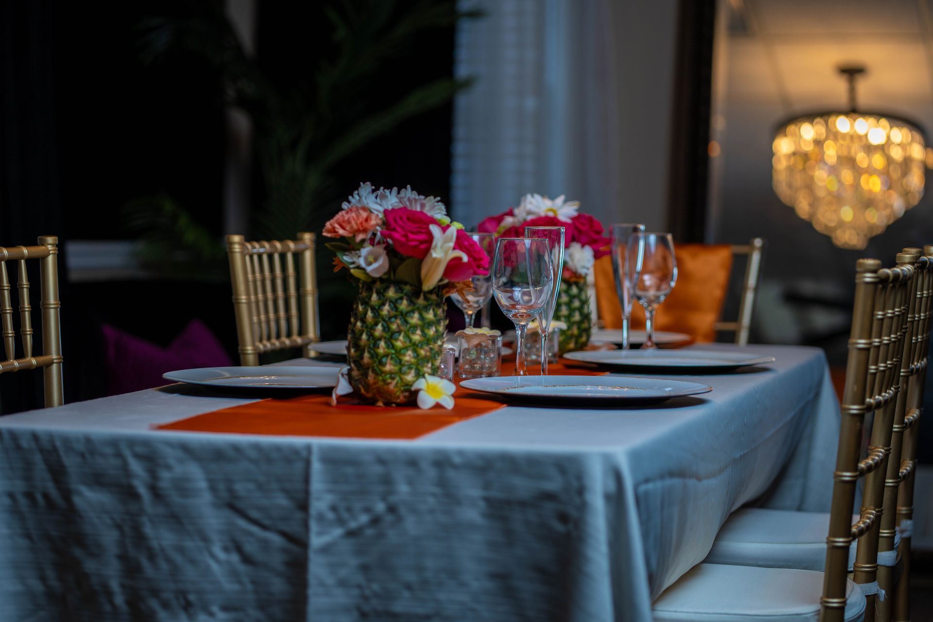 Formal dining table set with flowers, gold chairs, and orange accents.