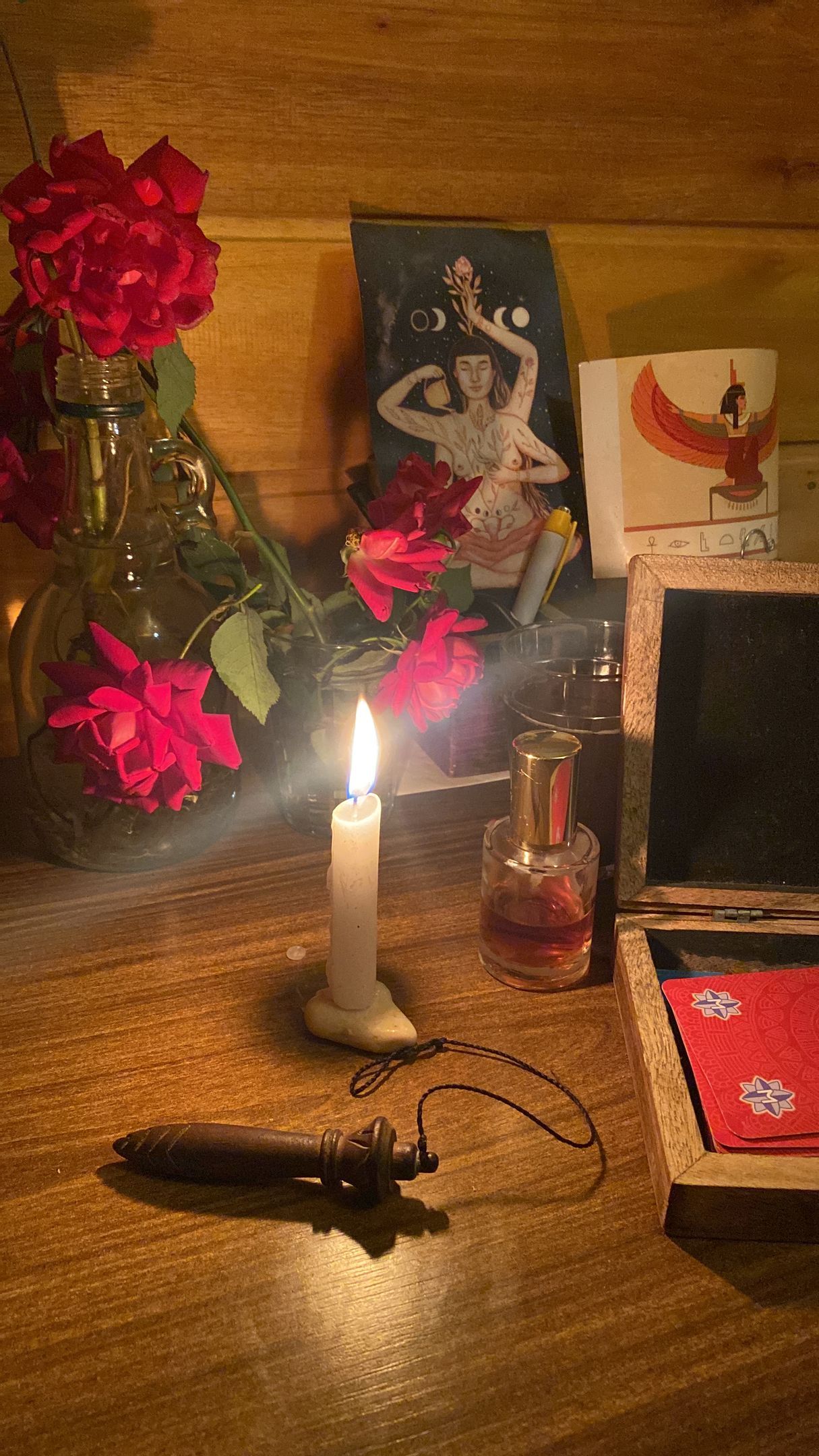 Altar iluminado por velas com rosas, cartões, um pêndulo e uma foto vintage.