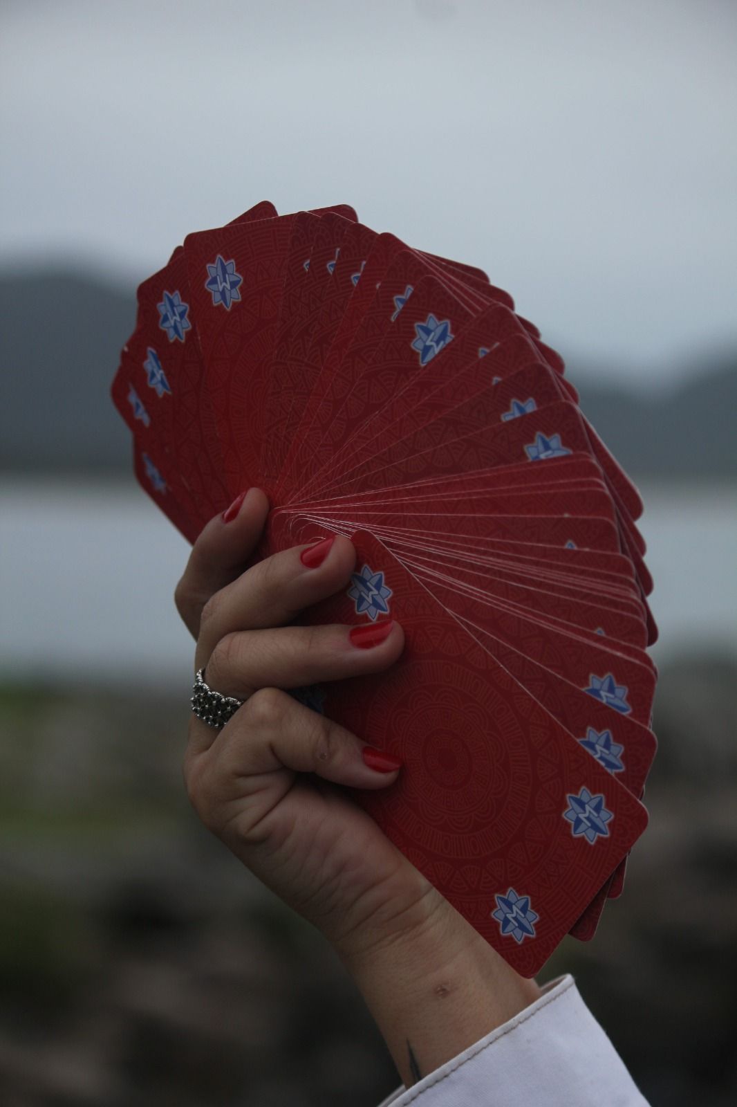Mão segurando cartas de tarô vermelhas em leque com desenhos de flocos de neve azuis contra um fundo externo desfocado.