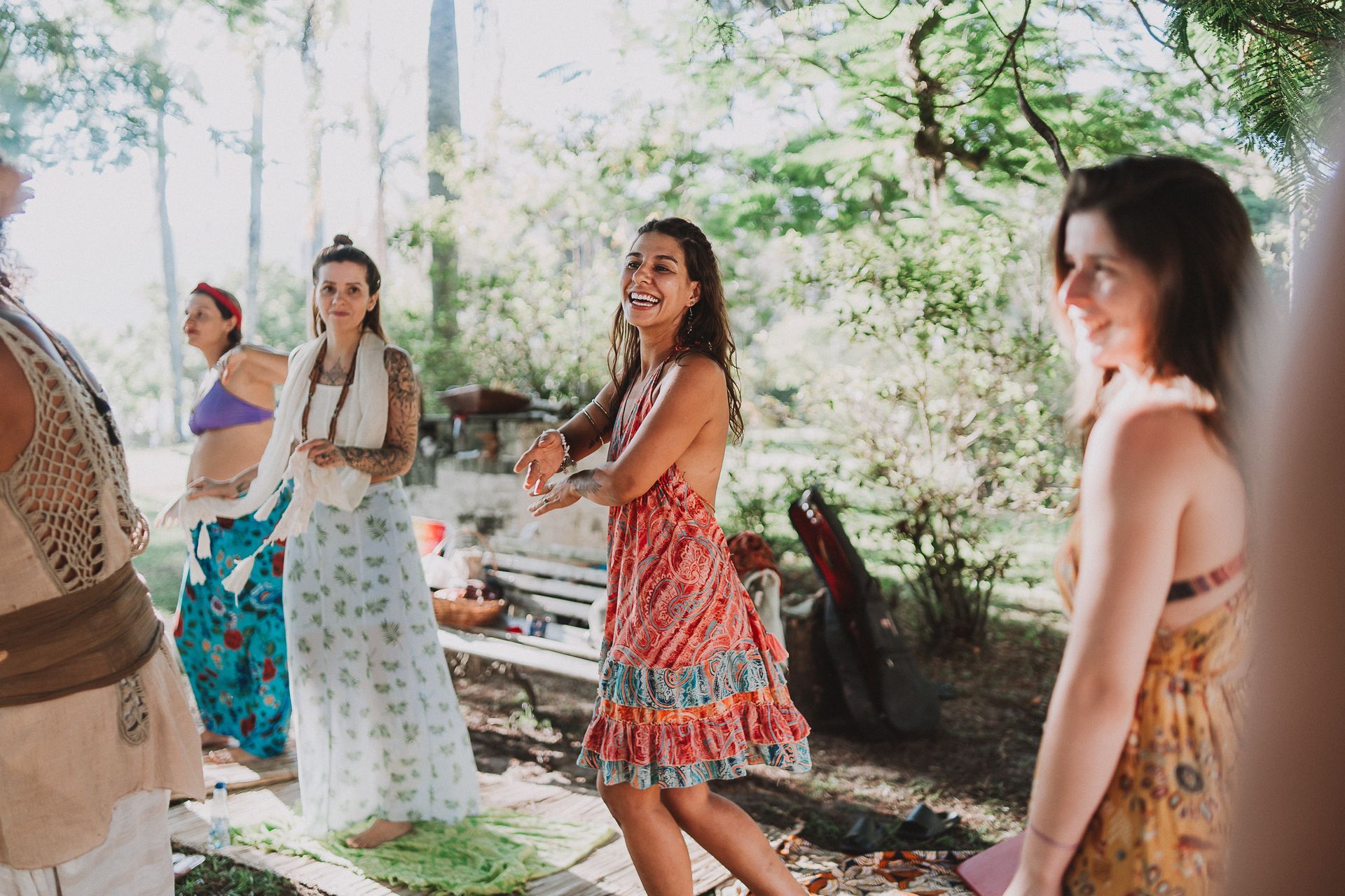 Grupo de mulheres dançando ao ar livre com vestidos coloridos, com árvores ao fundo.