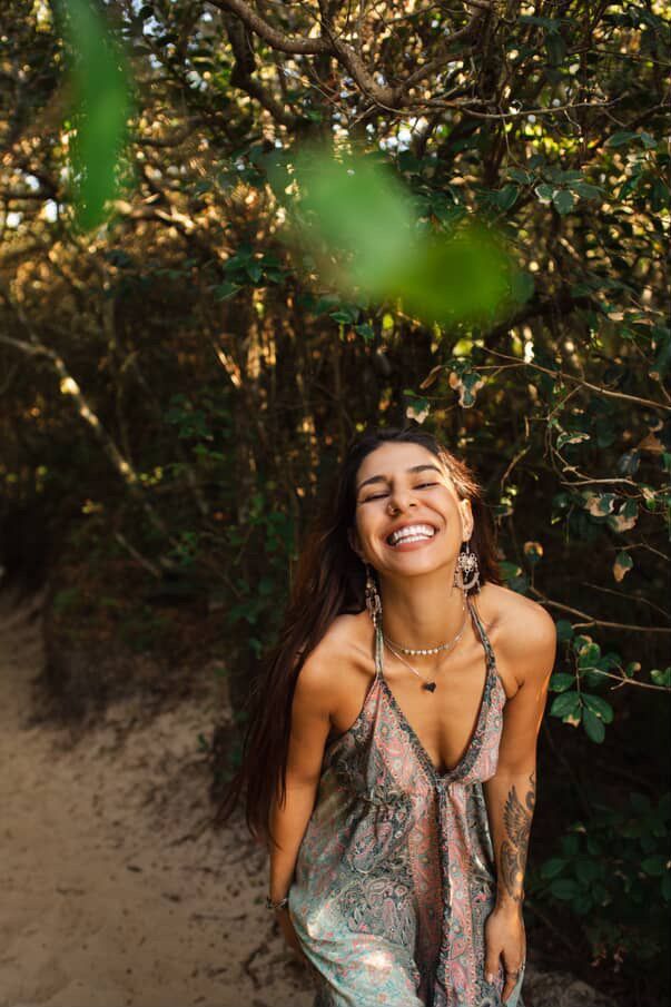 Mulher rindo alegremente em uma floresta, usando um vestido estampado.