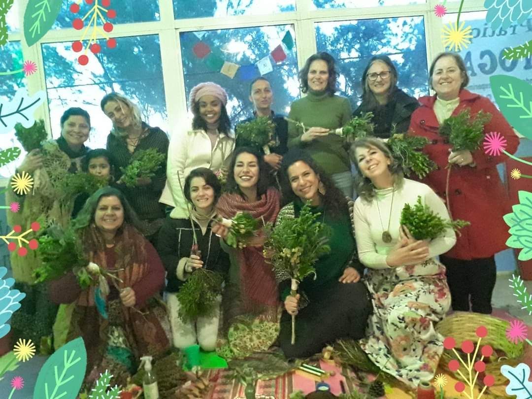 Grupo de mulheres sorrindo, segurando plantas verdes, posando ao ar livre.